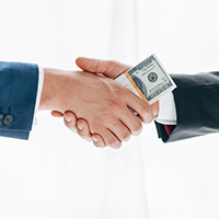 Two businessmen shaking hands with money.